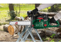 Green cordless chainsaw cutting a wooden log on a sawhorse in an outdoor setting.