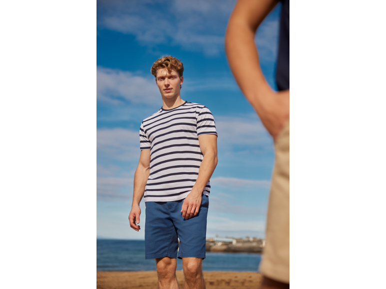Man in a striped t-shirt and blue shorts at the beach.