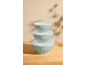 Stack of three light green mixing bowls with white lids on a wooden surface.