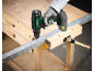 Green and black cordless drill drilling a metal bar on a wooden workbench.