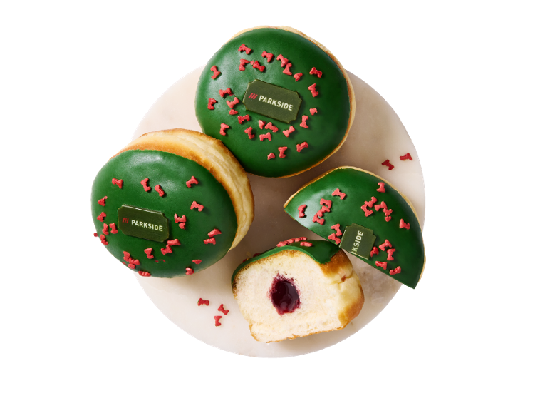 Four green-glazed donuts with red sprinkles, one cut open revealing a filling.
