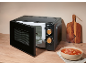 Black microwave with open door, bowl of soup, and wooden cutting board in a kitchen.