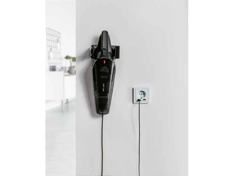 Black cordless handheld vacuum cleaner, hanging on the wall and charging.