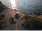 Two tents and two people camping by the sea at sunset.