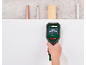 A handheld locator detecting hidden pipes, wires, and wooden beams behind a wall.