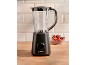 Black blender with a clear jug and berries in a bowl on a wooden countertop.