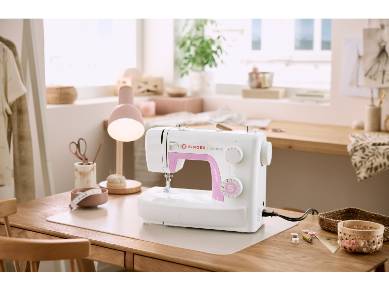 White sewing machine with pink accents on a sewing desk.