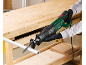 Electric reciprocating saw cutting a metal pipe on a wooden workbench.