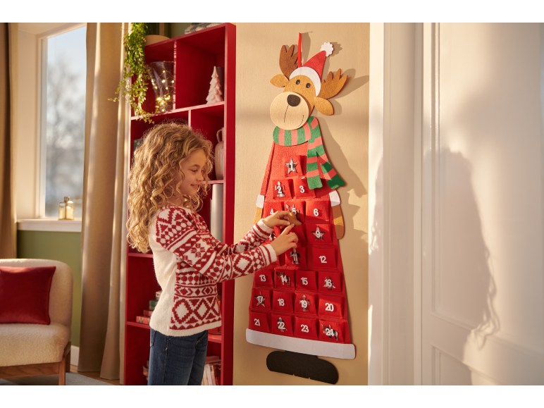 Girl with curly hair opening a pocket on a reindeer-shaped Christmas advent calendar.