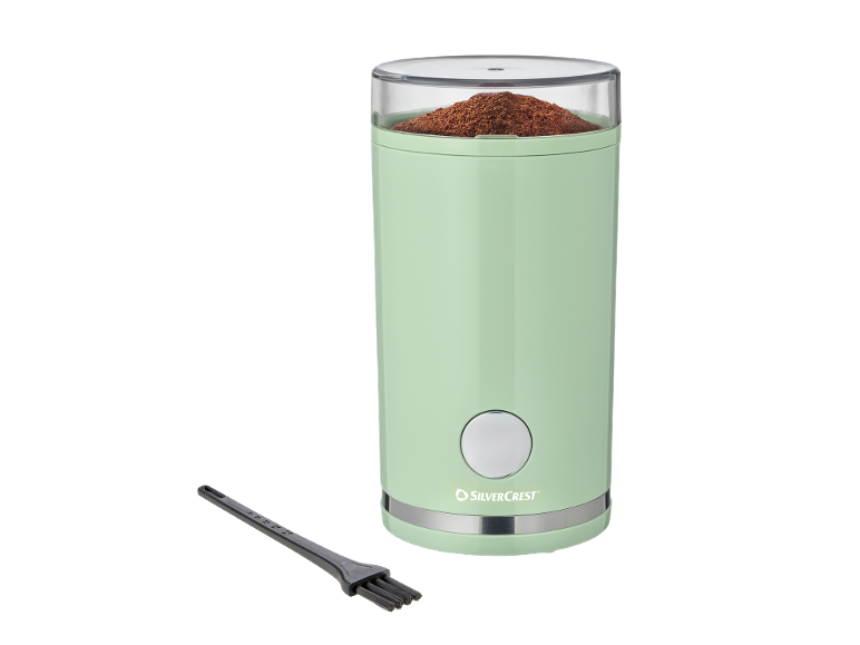Mint green coffee grinder with ground coffee and a cleaning brush.