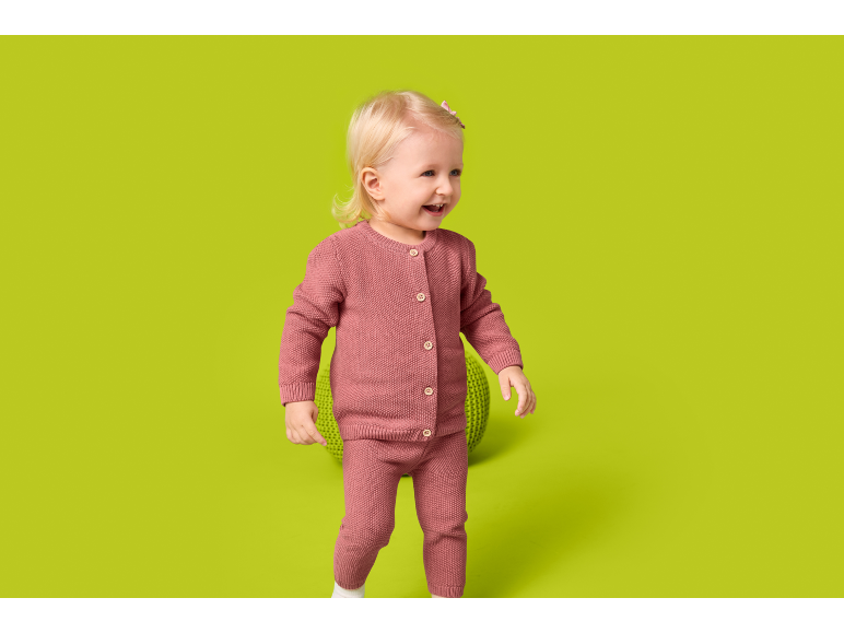 Toddler in a pink knitted set, smiling and looking to the right.