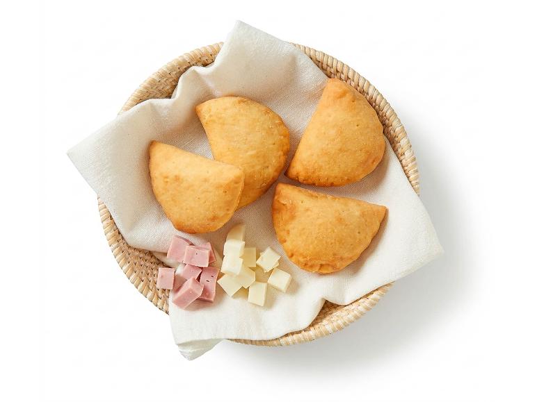 Golden empanadas in a basket with ham and cheese cubes.