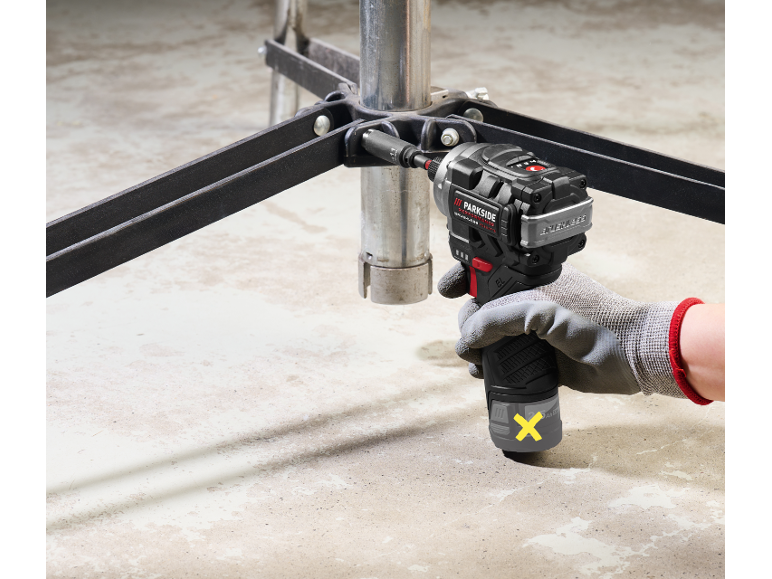 Cordless impact driver fastens metal construction to concrete floor.