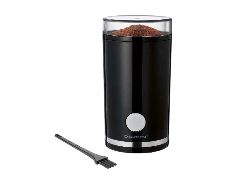 Black coffee grinder with a transparent lid filled with ground coffee, and a cleaning brush.