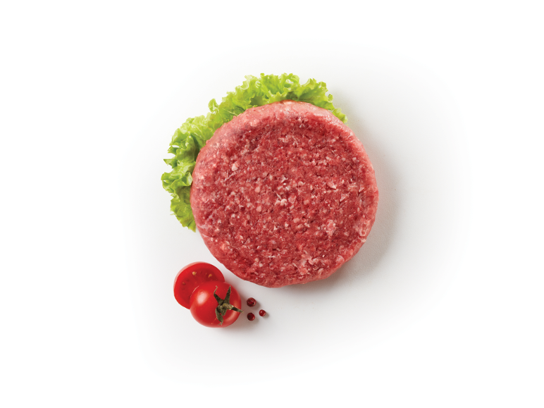 Raw burger patty with lettuce and cherry tomatoes on a white background.