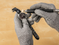 Grey gloves polishing a wristwatch with a rotary tool on a wooden table.