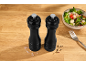 Black salt and pepper mills on a wooden table with salad and a fork.