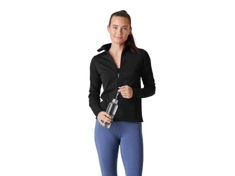 Woman in black sports jacket and blue leggings holding a water bottle.