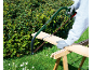 Man cutting a wooden board with a saw on a wooden sawhorse in the garden.
