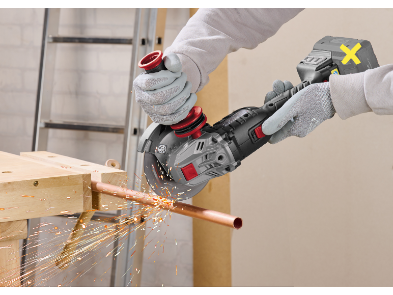 Man cutting a copper pipe with a cordless angle grinder, generating sparks.