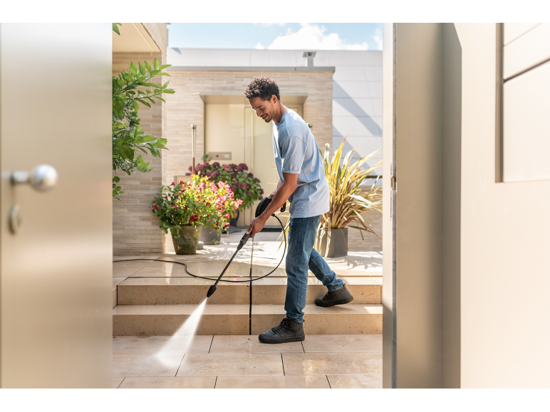 Man cleaning a patio with a pressure washer, with potted plants in the background.