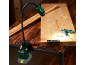 Work light with clamp illuminates a wooden board with tools and screws.