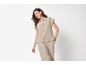 Woman in a beige short-sleeved button-up shirt and matching trousers, smiling.