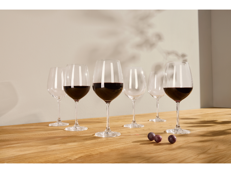 Wine glasses with red wine and empty glasses on a wooden table, with grapes.