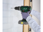 Gloved person drilling into a white brick wall with a cordless drill.