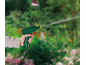 Hand holding a green garden sprayer, watering plants in a blurred garden background.