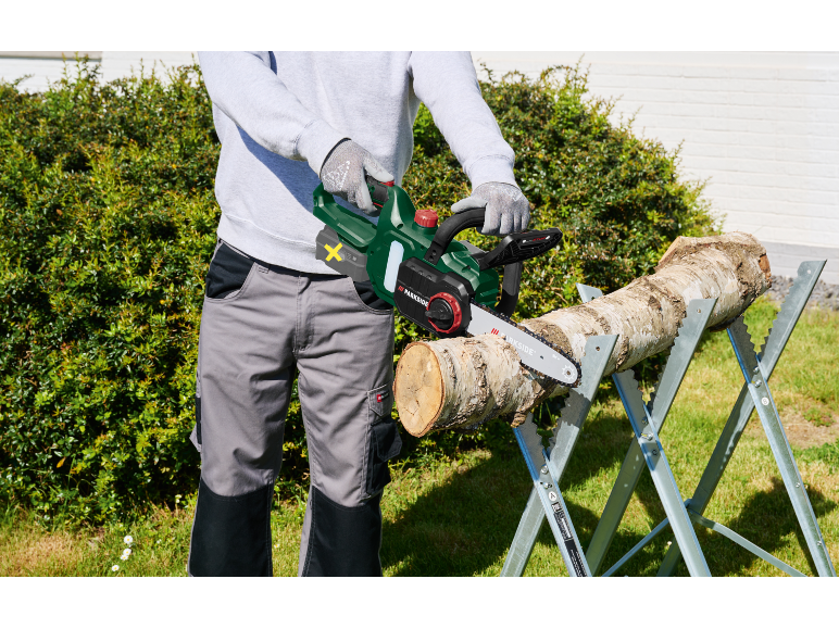 Man cutting a log with a chainsaw on a sawhorse.