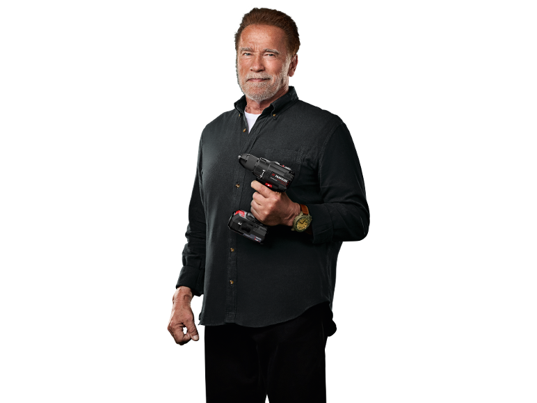 Arnold Schwarzenegger holds a cordless drill driver against a black background.