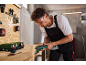 Man uses a multi-tool on a wooden board in a workshop.