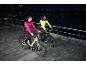 Two cyclists in reflective jackets riding bikes at night along a river.