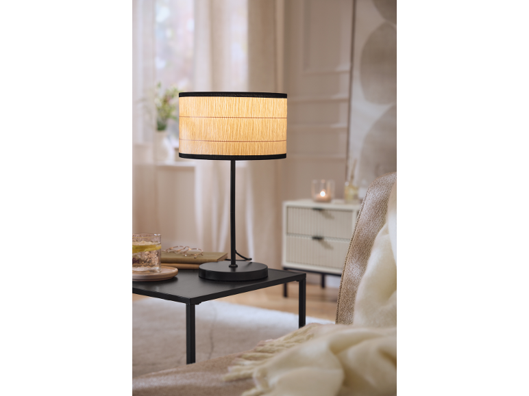 Table lamp with a woven shade on a black side table in a cozy living room.