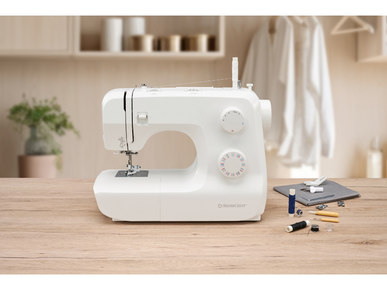 White sewing machine on a wooden table with threads and sewing accessories.
