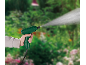Hand holding a green sprayer spraying water in a garden.