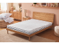 Bedroom with white mattress, pillows and duvet on a pouf, and wooden furniture.