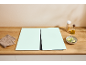 Wooden kitchen countertop with two light green cutting mats, a cloth, oil, and a bowl of zucchini.