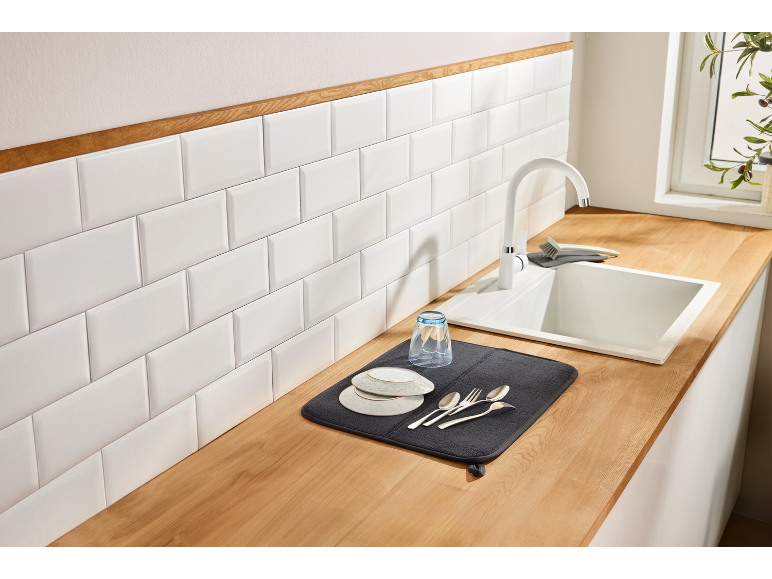 Kitchen counter with white sink, faucet, and dish drying mat with plates and cutlery.