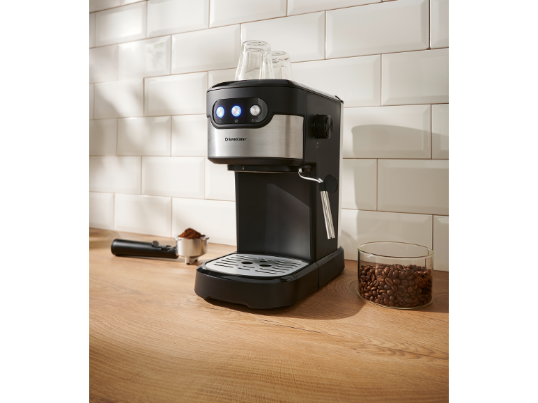 Black and silver espresso machine with coffee beans and ground coffee on a wooden counter.