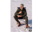 Man in green tracksuit and brown boots sitting on a chair in the snow.