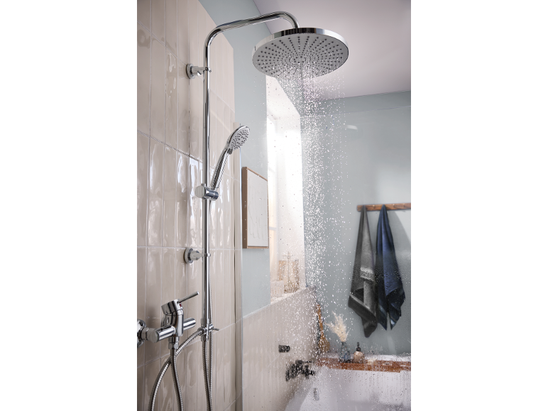 Chrome rain shower and hand shower in a modern bathroom with light tiles.