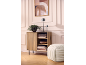 Wooden cabinet with a plant, lamps, and books, next to a pouf, against a wall with art.