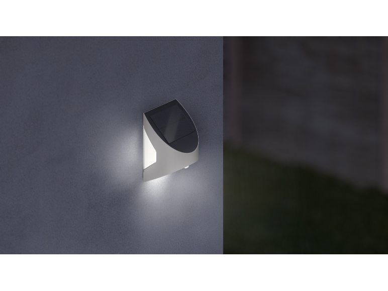 Solar-powered outdoor wall light illuminating a dark wall.