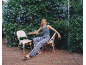 Woman in patterned trousers and wedge sandals sitting in a flowery patio.