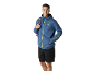 Smiling man in blue hoodie and black shorts, with a backpack over his shoulder.