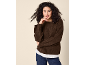 Woman in a brown sweater and jeans, with her hand on her chin.