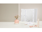 Lighted tri-fold makeup mirror with a vase of flowers and beauty accessories.