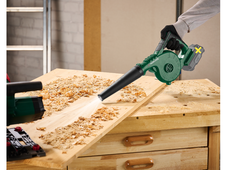 Cordless blower cleaning wood shavings from a workbench.